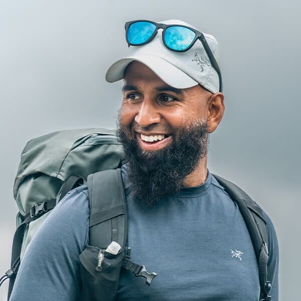 Haroon Mota smiling on a mountain trail, wearing Arc'teryx gear and a backpack — the founder of Muslim Hikers and Active Inclusion Network